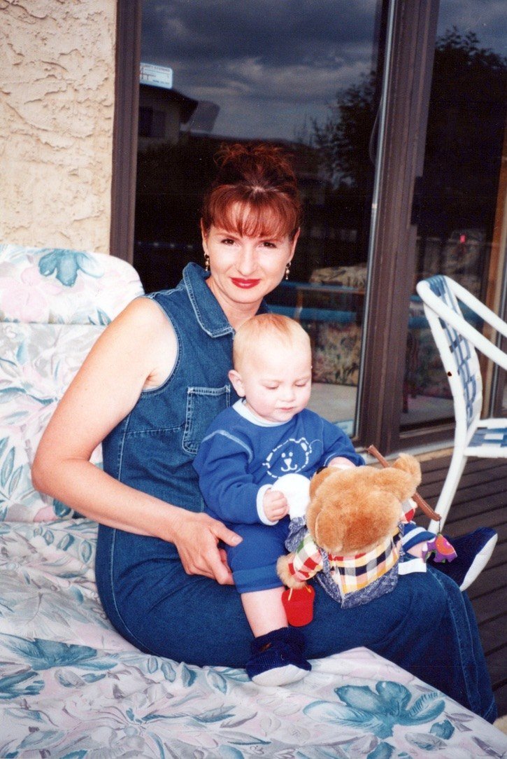 Gloria Pidwerbesky on a patio, holding a baby and a teddy bear on her lap